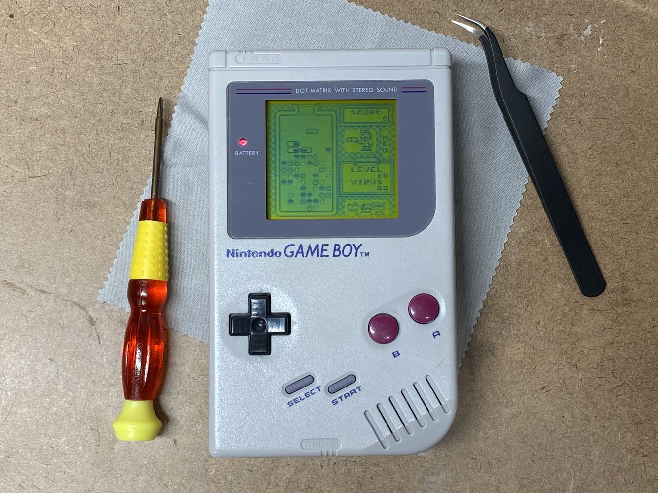 Game Boy showing Dr. Mario. System is on a workbench next to a screwdriver and tweezers