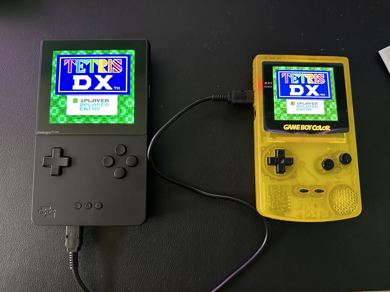 Black Analogue Pocket next to a yellow Game Boy Color. Both show Tetris DX title screen and are linked with a cable.
